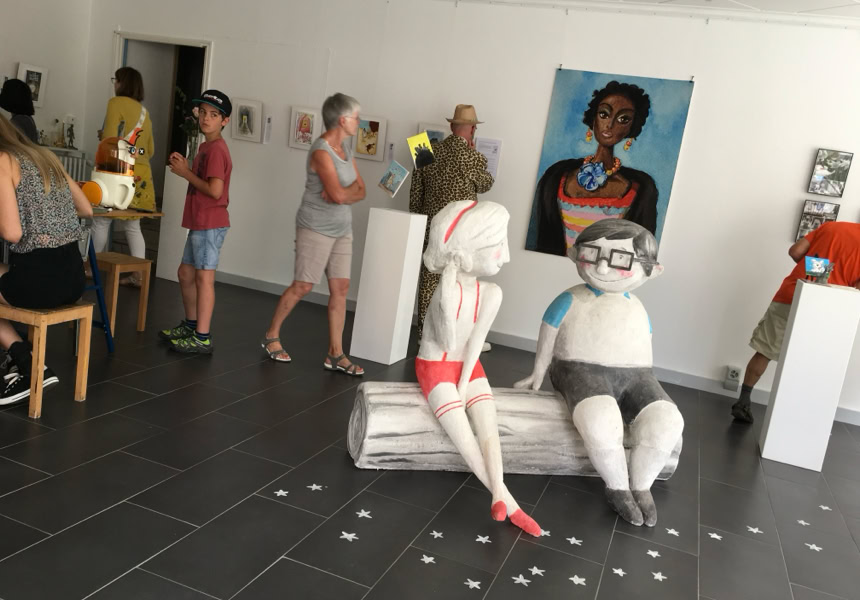 Galerie d'art avec sculptures sur socles blancs et plusieurs peintures accrochées au mur.