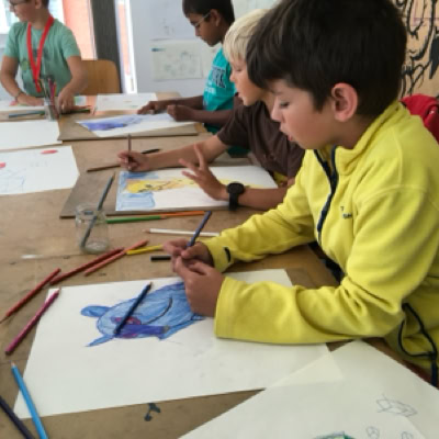 Des enfants assis à une table en train de dessiner avec des crayons de couleur.