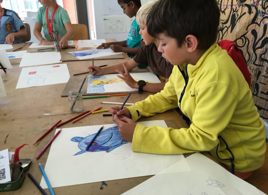 Des enfants assis à une table en train de dessiner avec des crayons de couleur.