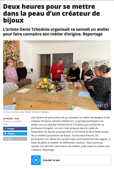 Des personnes assises autour d'une table, travaillant sur des projets de création de bijoux, avec divers outils et matériaux dispersés sur la table. Une personne debout semble donner des instructions.
