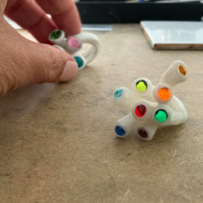 Travail à la main d'une bague en résine blanche avec des perles colorés, posé sur une surface en bois.