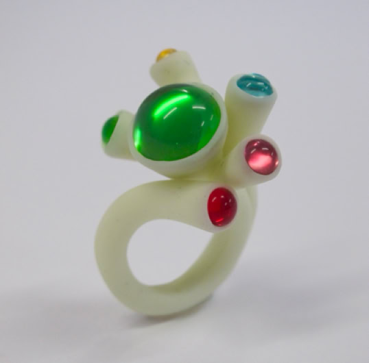 Bague blanche avec des pierres colorées vertes, rouges et bleues.